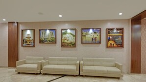 Eine Lobby mit drei beigefarbenen Sofas, einem Marmorboden und gerahmten Bildern an der Wand.