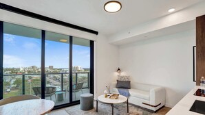 Un soggiorno moderno con un divano bianco, un tavolino rotondo e un balcone con vista sulla città.