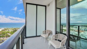 Ein Balkon mit zwei weißen Korbstühlen, einem kleinen Tisch und Blick auf das Meer und die Stadt.