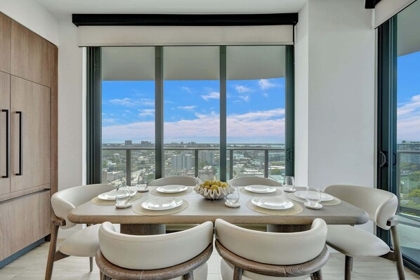 A dining area with a table set for four, large windows, and a city view.
