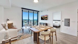 A modern living room with a dining area, a sofa, a coffee table, and a view of the city.