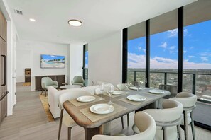 Un coin repas avec une table dressée pour six personnes, de grandes fenêtres et une vue sur le paysage urbain.