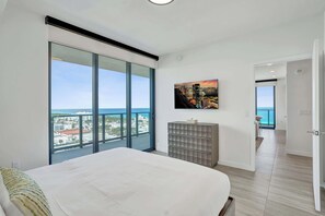 Une chambre dotée d’un grand lit, offrant une vue sur la ville grâce à une porte coulissante, agrémentée d’une œuvre d’art fixée au mur et comprenant un meuble de rangement.