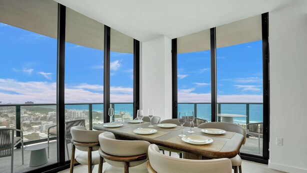 Un comedor con una mesa lista para cuatro, ventanas amplias y vistas a la ciudad y al mar.