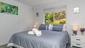 A bedroom with a large bed, two bedside tables, a window with a view of trees, and a painting on the wall. - Tranquil Haven The Perfect Blue Mountains Escape (KATOOMBA)