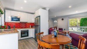 A compact kitchen with a microwave, oven, and refrigerator. There is a dining area with a round wooden table and chairs. - Tranquil Haven The Perfect Blue Mountains Escape (KATOOMBA)