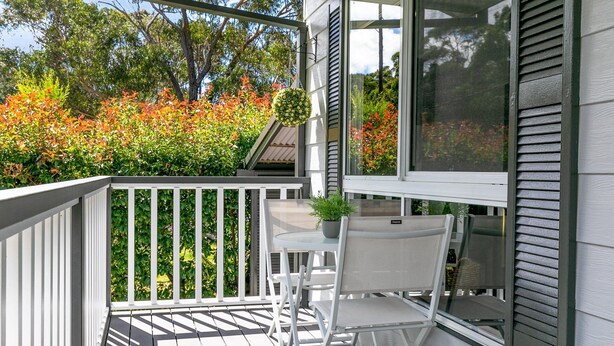 A covered outdoor seating area with white chairs and a table, surrounded by a white railing. - Tranquil Haven The Perfect Blue Mountains Escape (KATOOMBA)