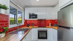 A modern kitchen with white cabinets, a red-tiled backsplash, stainless steel appliances, and a window with a view of greenery. - Tranquil Haven The Perfect Blue Mountains Escape (KATOOMBA)