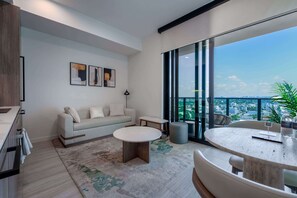 A modern living room with a sofa, coffee table, and a view of the city through large windows. - 21st Floor 1BR Beach Access, Pool & Skyline (Miami Beach)