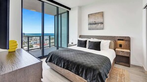 A bedroom with a large bed, a nightstand, a bedside table, a window with a city view, and a painting on the wall. - 21st-Floor 2BR/1BA | Views, Pool & Gym, 72 Park (Miami Beach)