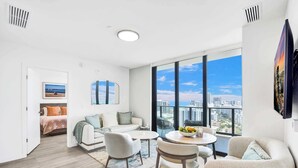 A modern living room with a large window, a dining area, and a bedroom. - Penthouse Perfect | 2BR/2BA, Ocean Air & Views (Miami Beach)