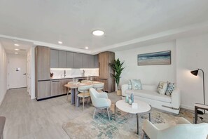 A modern living room with a sofa, a dining table, and chairs. There is a kitchen area with cabinets and a countertop.