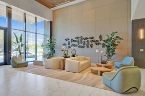 A modern lobby with large windows, a wall-mounted art installation, and several seating areas with plants.