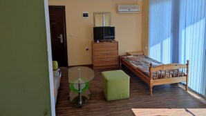 A small, well-lit room with a bed, a wooden dresser, a television, and a window with blinds. - Oceonviev Retreat (Varna)