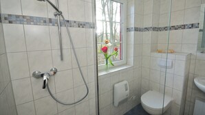 A bathroom with a shower, toilet, and window with flowers. - Waldhaus Zwenzow (Userin)