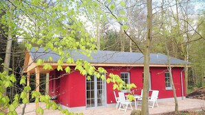 A red wooden cabin with a covered patio, white chairs, and a dining table. - Waldhaus Zwenzow (Userin)