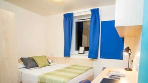 A compact hotel room with a bed, a desk with a laptop, a notebook, and a desk lamp. - For Students Only Queen's Hospital Close near Birmingham City Centre (Birmingham)