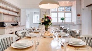 A dining area with a wooden table set for six, white chairs, a central vase with flowers, and a hanging light fixture. - Luxurious 4 bedroom apartment @Pickwell Manor on North Devon Coast near Croyde (Georgeham)
