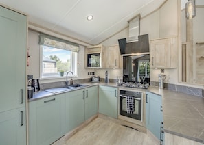 A modern kitchen with light green cabinets, a built-in oven, and a window with a view of greenery.