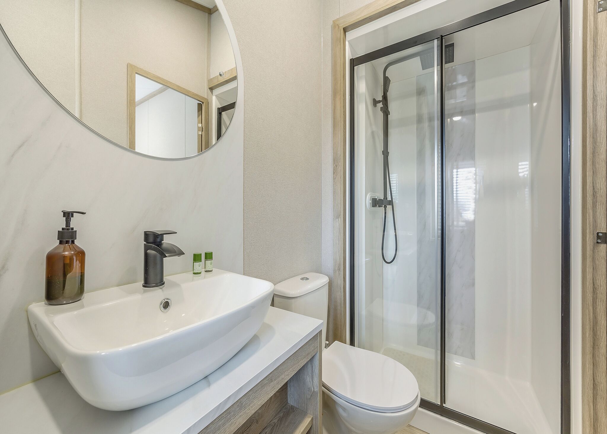 A bathroom with a white sink, a toilet, a shower enclosure, and a mirror.