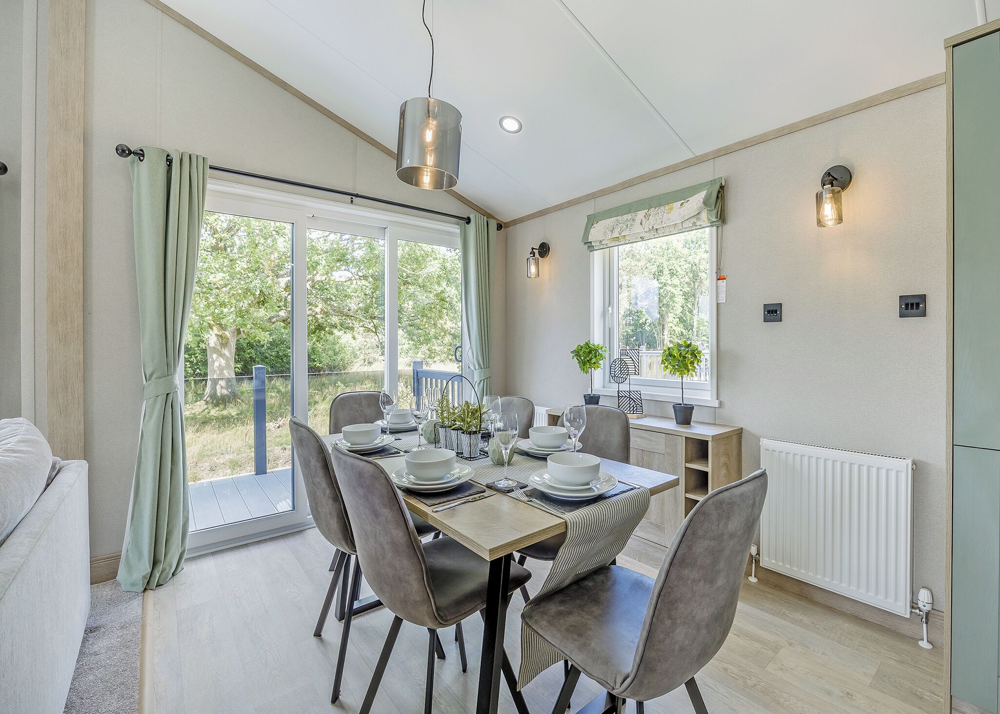 A dining area with a table set for four, chairs, a hanging light fixture, a window with a view, and a radiator.