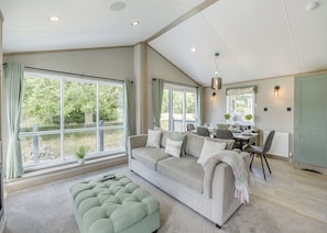 A spacious living room with a large window, a sofa, a dining table, and a kitchen area.
