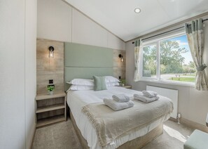 A bedroom with a bed, bedside tables, a window with curtains, and a view of the outdoors. - 2 bedroom accommodation in Woodhall Spa (Woodhall Spa)