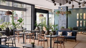 A modern indoor space with round tables, chairs, and a sofa. There are potted plants and a wall with decorative skateboards. - Walk to Gaslamp Quarter + Rooftop Pool & Dining (San Diego)
