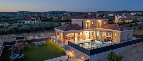 A modern house with a swimming pool, a patio, and a view of the surrounding landscape.