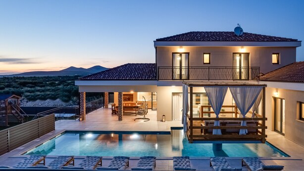 A modern house with a swimming pool, outdoor seating, and a view of the mountains.