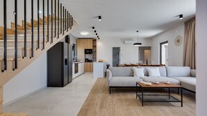A modern living space with a staircase, a kitchen, a dining area, and a sofa.