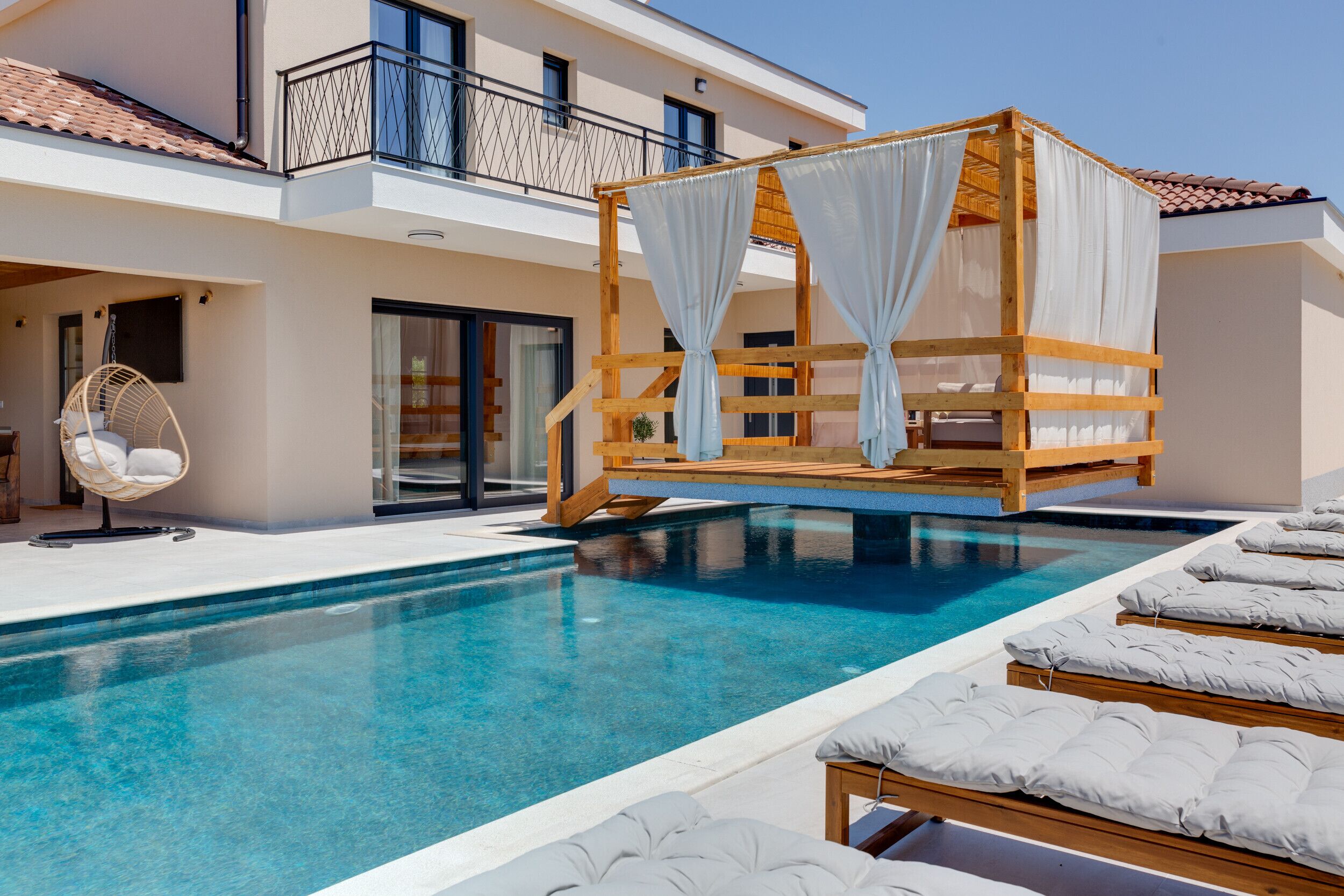 A pool area with a wooden canopy and lounge chairs.