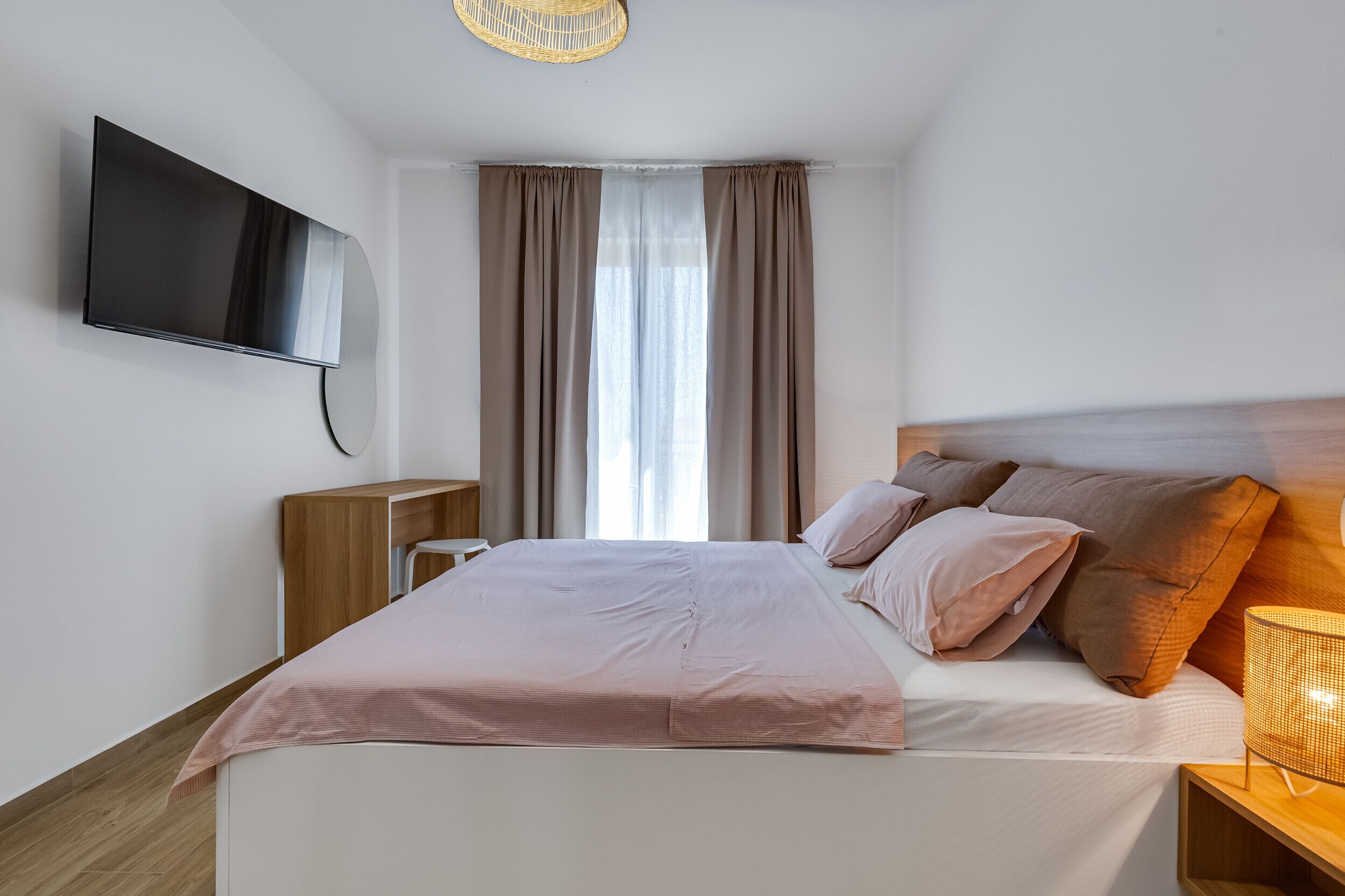 Une chambre à coucher moderne, avec un lit, un téléviseur fixé au mur, une table de chevet et une fenêtre avec des rideaux.