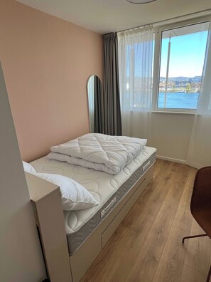 A bedroom with a bed, a window with a view of a body of water, a mirror, and a chair. - Comfort Studio in a Premium Residence- Sport/cinema (Huningue)