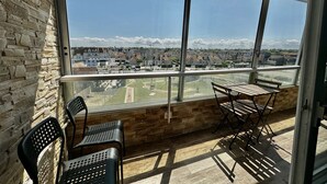 A balcony with a stone wall, two chairs, a table, and a view of a residential area. - Les pieds dans l'eau - south-facing loggia (Courseulles-sur-Mer)