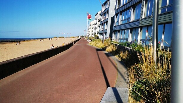 A coastal road with a beach on one side and a row of buildings with balconies. - Les pieds dans l'eau - south-facing loggia (Courseulles-sur-Mer)