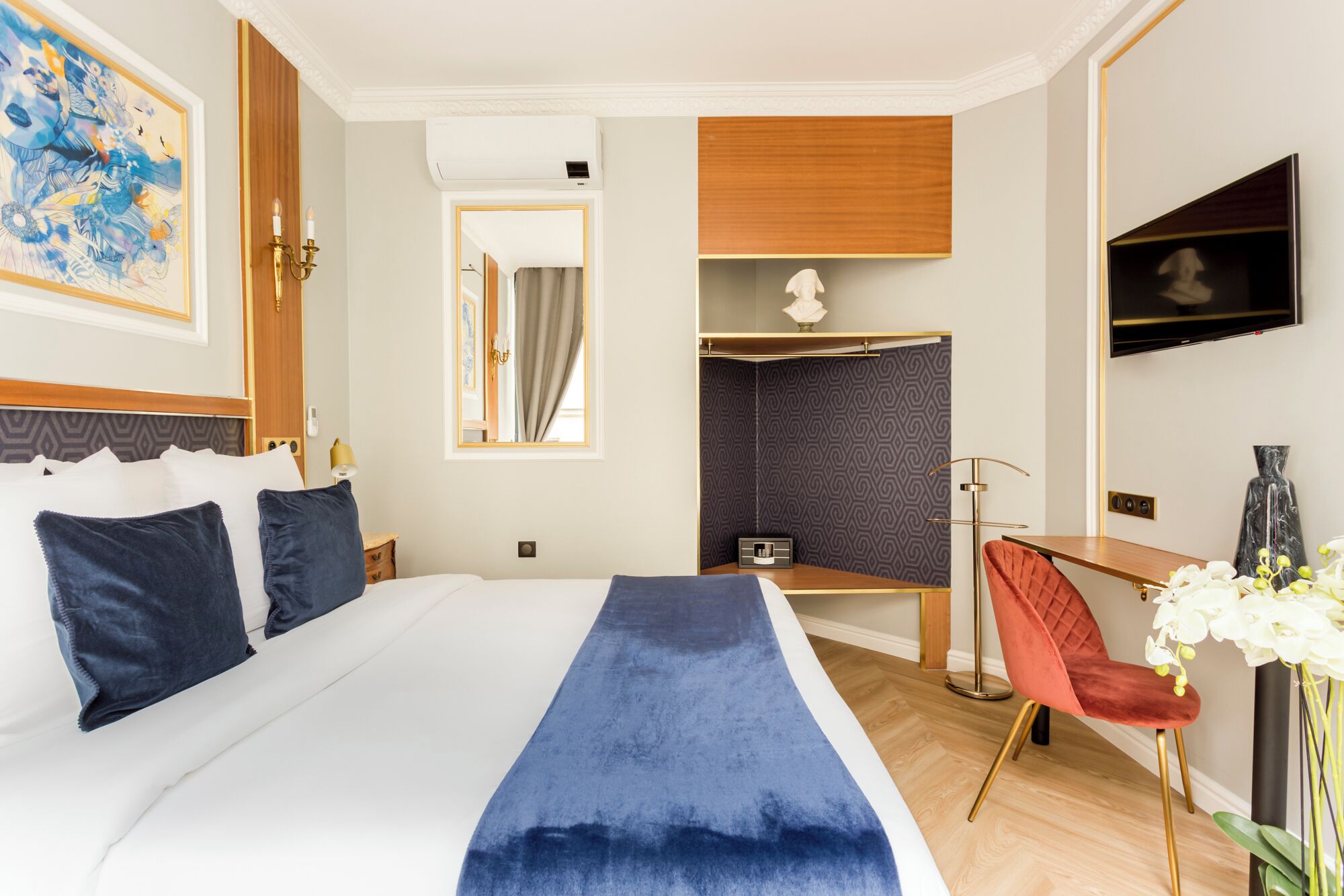 A hotel room with a large bed, a desk, a chair, a TV, and a mirror.