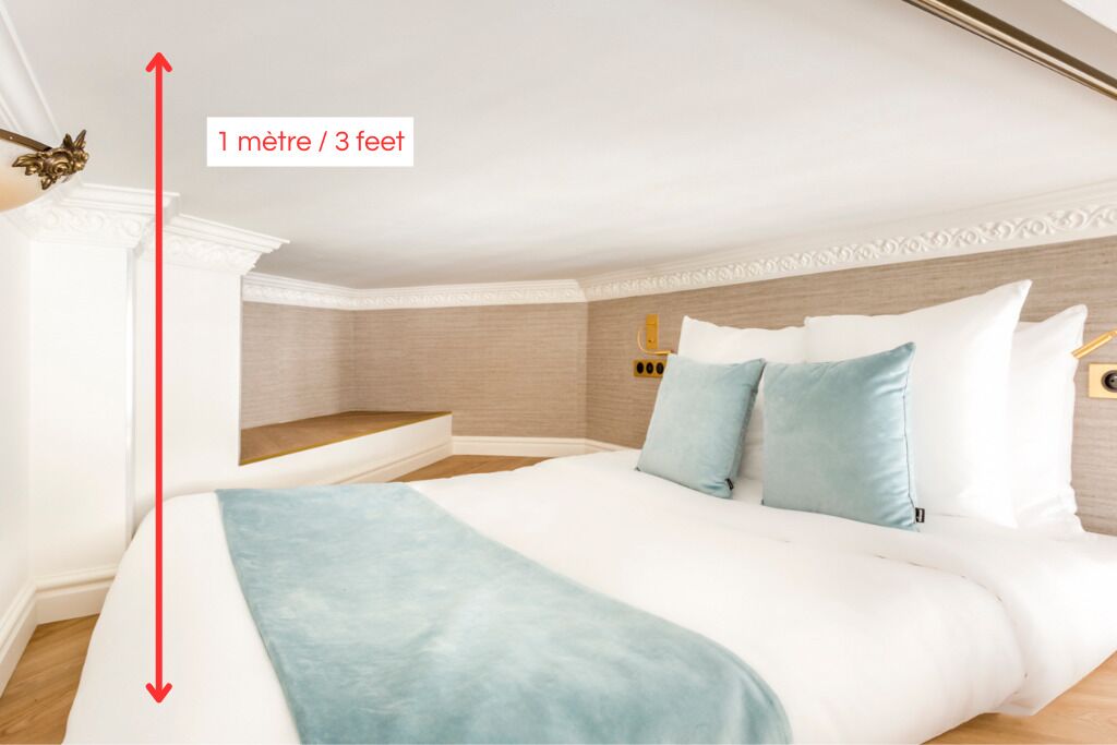 A bedroom with a bed, pillows, and a nightstand. A red arrow indicates the room's height.