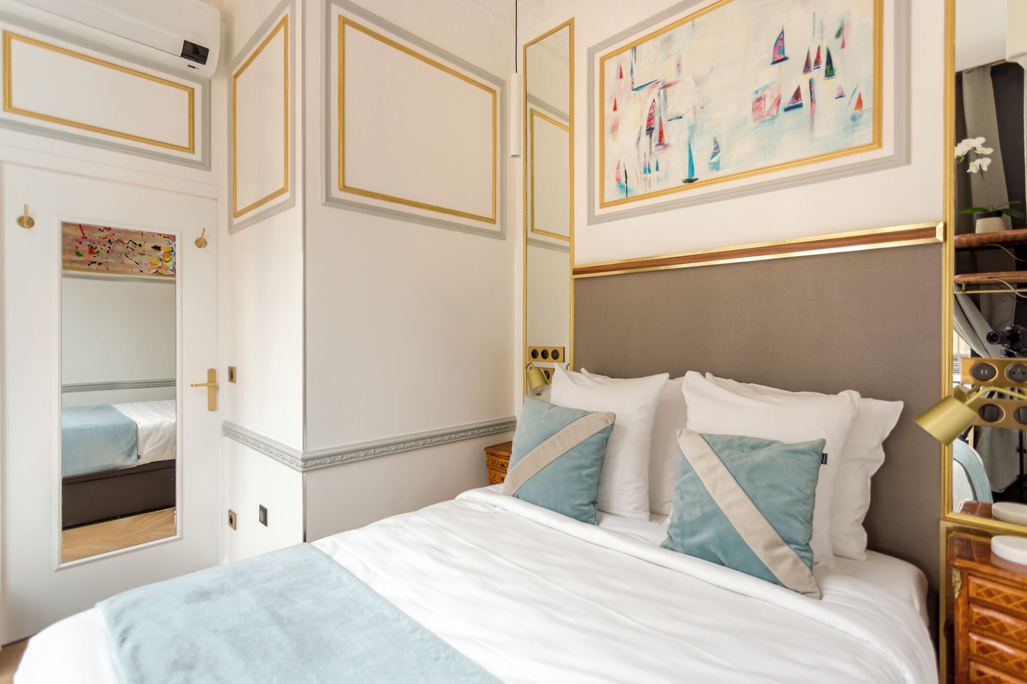 Une chambre à coucher avec un lit, des tables de chevet, un miroir et un tableau accroché au mur.