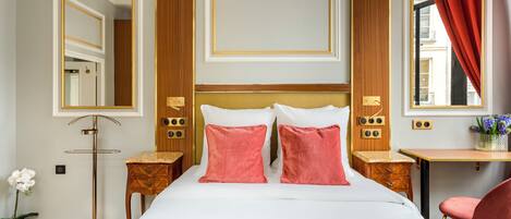 Ein Hotelzimmer mit einem großen Bett, zwei Nachttischen, einem Schreibtisch, einem Stuhl und einem Vorhangfenster.