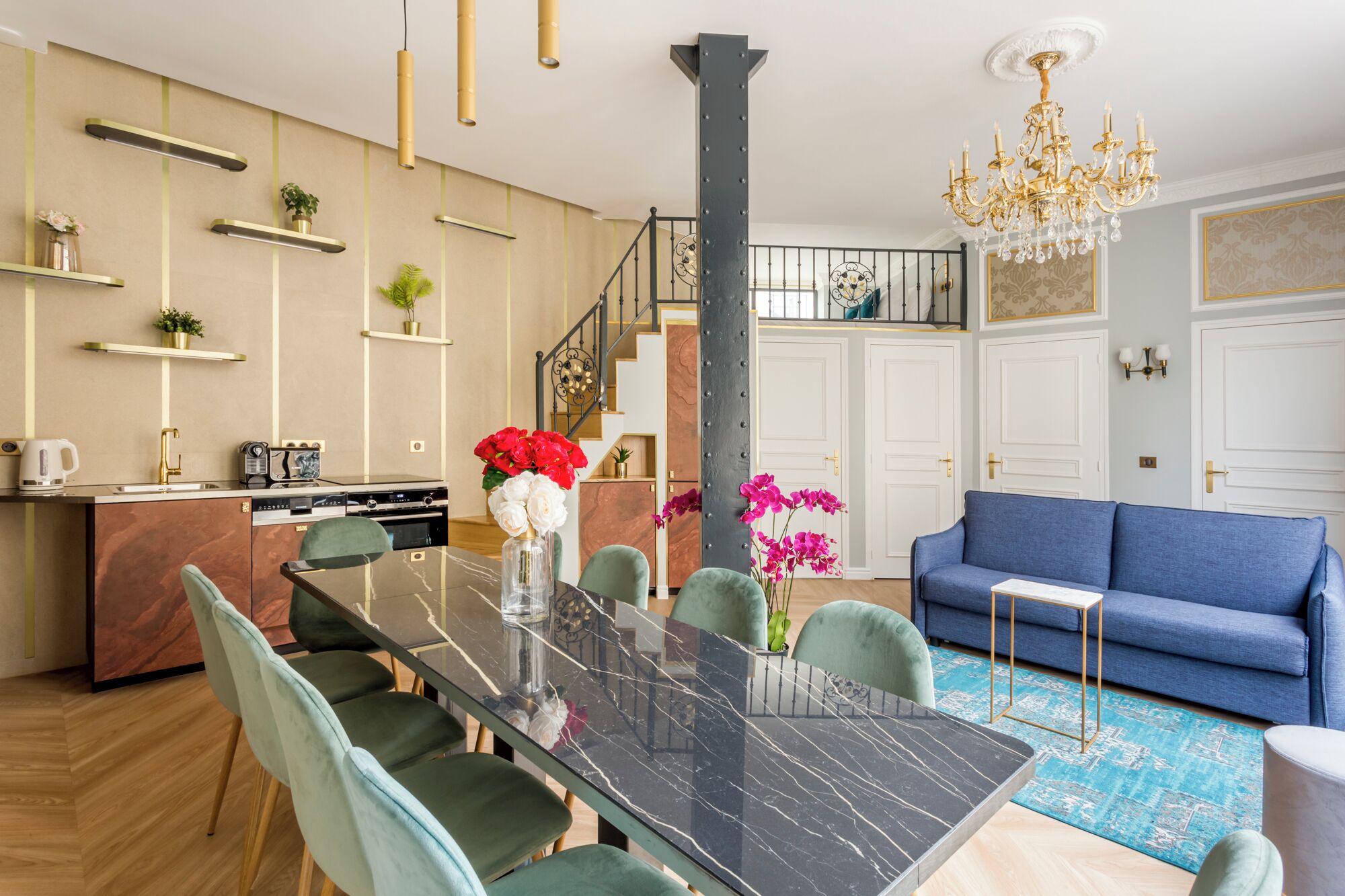 A modern kitchen with a marble countertop, a dining table with chairs, a blue sofa, and a chandelier.