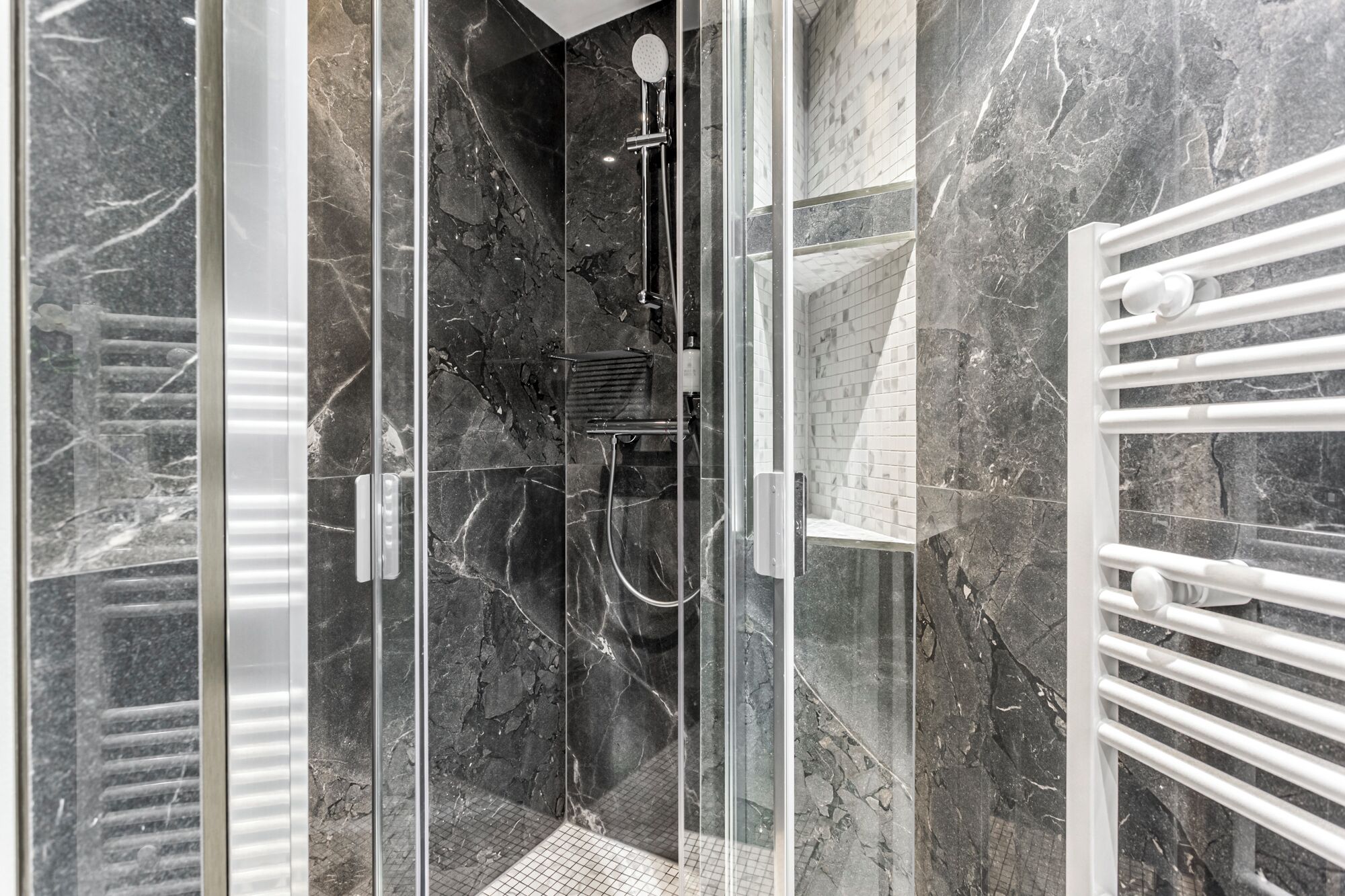 Une salle de bain moderne avec une douche à parois de verre, des murs en marbre et un porte-serviettes blanc.