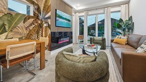 A modern living room with a flat-screen TV, a dining area with a wooden table and chairs, and a comfortable seating area with a sofa and armchair. - `Bali in Houston`/8BR/8Bath/Heated Pool/Sleeps 23 (Houston)