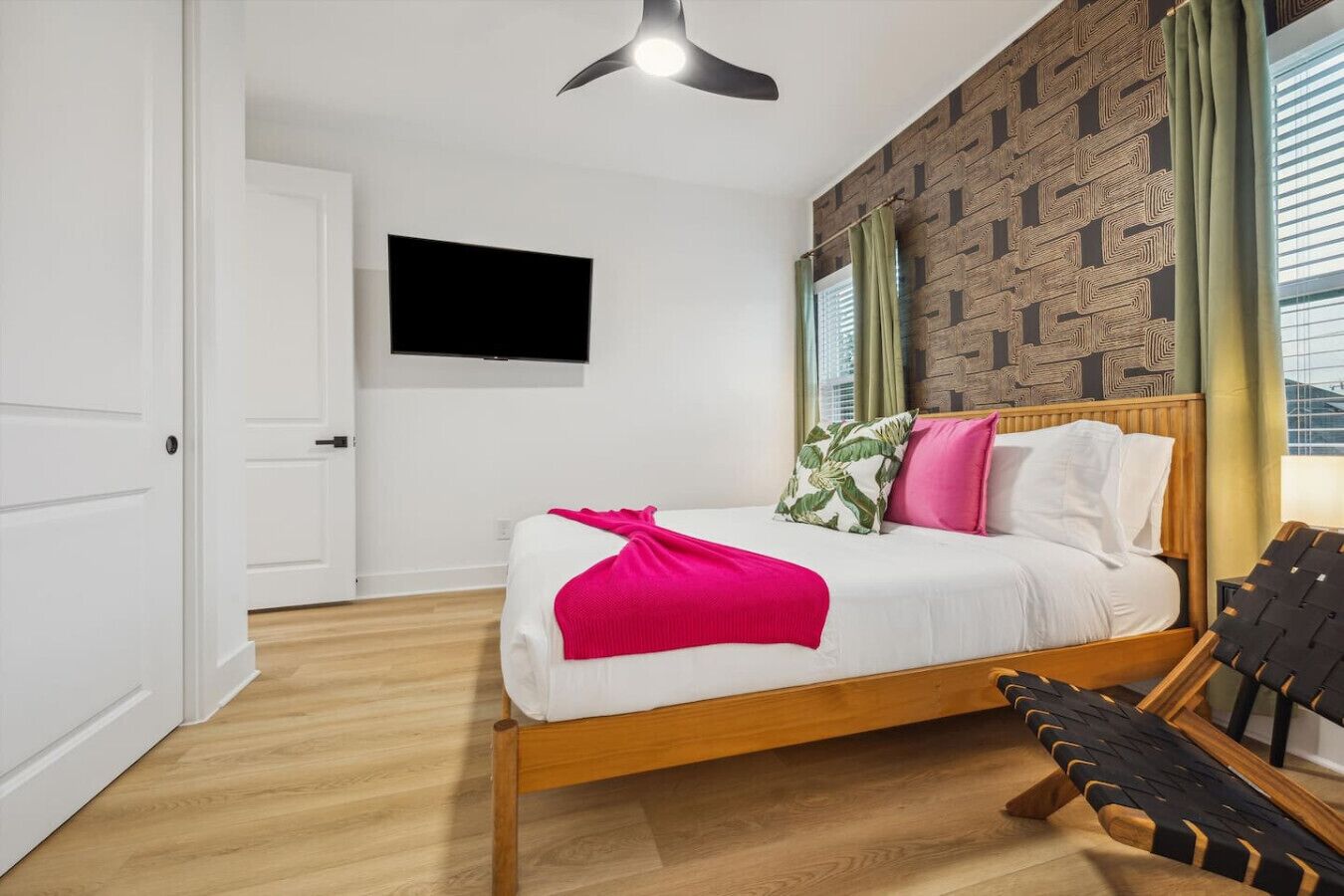 A modern hotel room with a wooden bed, a flat-screen TV, and a patterned wall.
