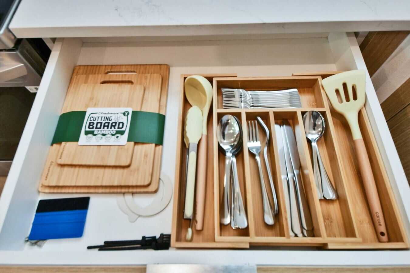 Un cajón con una tabla de cortar, varios utensilios de cocina y una espátula.