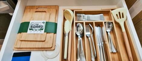 Un cajón con una tabla de cortar, varios utensilios de cocina y una espátula.