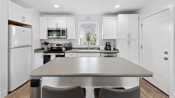 A modern kitchen with white cabinets, a stainless steel refrigerator, a microwave, and a large island with seating.