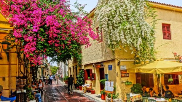 A narrow street lined with buildings, some with outdoor seating and tables, and a cyclist in the distance. - Plaka City Studio – Walk to Syntagma by ΜΡS (Athina)