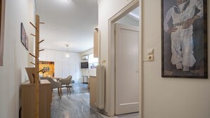 A hallway with a wooden coat rack, a dining area with chairs and a table, and a framed artwork on the wall. - Plaka City Studio – Walk to Syntagma by ΜΡS (Athina)