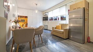 A modern kitchen with a built-in refrigerator, a dining area with chairs, a sofa, and a bookshelf. - Plaka City Studio – Walk to Syntagma by ΜΡS (Athina)